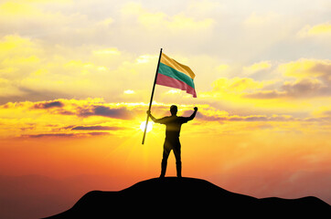 Lithuania flag being waved by a man celebrating success at the top of a mountain against sunset or sunrise. Lithuania flag for Independence Day.