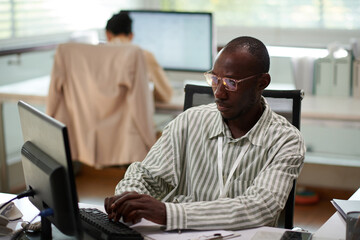 Pensive businessman in glasses filling document at his office desk