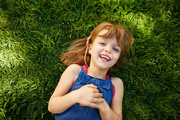 Fototapeta premium Child, portrait and grass with smile or above for relax holiday in countryside for summer vacation, nature or park. School kids, face and happy in California environment for laugh, sunshine or meadow