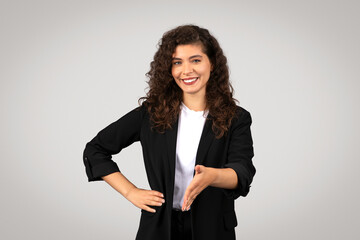 Smiling businesswoman extends her hand invitingly for handshake, grey background