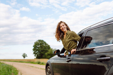 Young woman leaning out of the car window enjoying nature. Girl is resting and enjoying journey....
