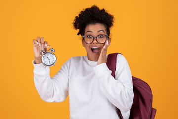 Shocked young black woman with backpack holding an alarm clock