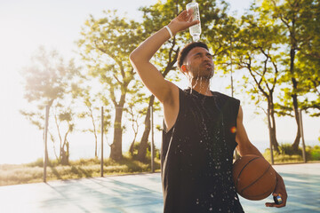 close-up portrait of young black man doing sports in morning, drinking water on basketball court