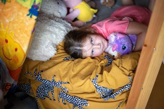 young girl laying on her bed surrounded by her teddies and hugging