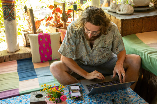 Young Man works on his laptop and phone in a restaurant in Northern Thailand, He is a digital Nomad working remotely.