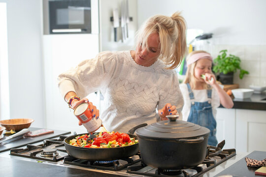 Attractive mother cooking a family meal, of healthy ingrediencies. Fresh tomatoes cooking in an iron pan. Her daughter laughing and playing in the background
