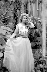 Black and white photo of a stunning girl in a wedding dress, blonde with long curls posing in nature. Women concept