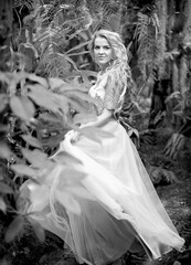 Obraz na płótnie Canvas Black and white photo of a stunning girl in a wedding dress, blonde with long curls circling in nature. Happiness concept