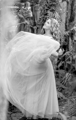 Black and white photo of a stunning girl in a wedding dress, blonde with long curls circling in nature. Happiness concept