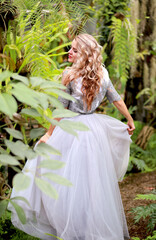 A beautiful blonde twirls in an elegant tulle dress in a botanical garden. Background greenery and tropical plants. Beauty and fashion concept