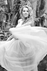 Black and white photo of a stunning girl in a wedding dress, blonde with long curls circling in nature. Happiness concept