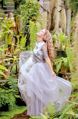 A beautiful blonde twirls in an elegant tulle dress in a botanical garden. Background greenery and tropical plants. Beauty and fashion concept