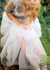 A girl sitting in a gray tulle dress in a botanical garden. Background greenery and tropical plants. Beauty and fashion concept