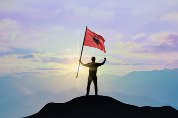 Albania flag being waved by a man celebrating success at the top of a mountain against sunset or sunrise. Albania flag for Independence Day.