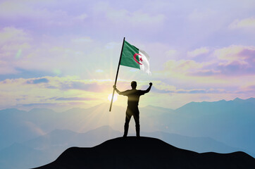 Algeria flag being waved by a man celebrating success at the top of a mountain against sunset or sunrise. Algeria flag for Independence Day.