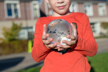 Child holding a glass globe in a public park, reflective light and clear glass