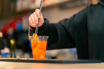 close-up of a young girl at the bar counter in the process of adding orange slices to cocktail with...