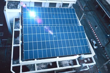 Urban Rooftop Solar Panels Overlooking Street :An aerial view of blue solar panels installed on a city building's rooftop, with a street view below.