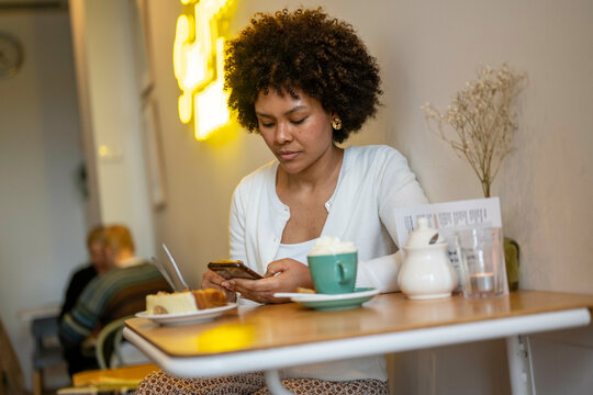 Attractive African woman with beautiful hair sitting with her phone at a coffee shop