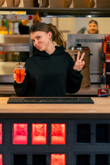 a young girl in a restaurant establishment stands at the bar counter with cocktail in her hand and smiles