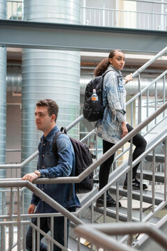 Male and female mixed race student standing at the stairs of her university looking positive