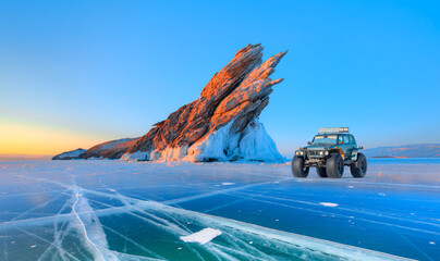 Ogoy island on winter Baikal lake with transparent cracked ice - A moving a thick-wheeled suv car on lake Baikal - Car tire tracks (trail) in fresh snow - Baikal Lake, Siberia