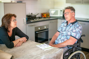 Husband in a wheelchair with wife sitting by his side helping him decide on what lunch he wants