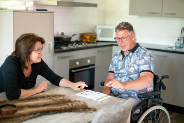 Husband in a wheelchair with wife sitting by his side helping him decide on what lunch he wants