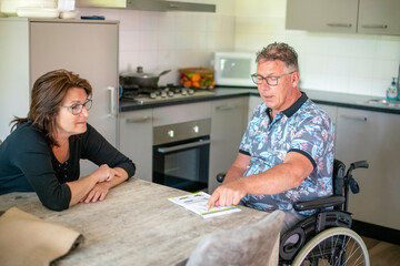 Husband in a wheelchair with wife sitting by his side helping him decide on what lunch he wants