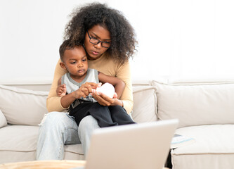 Afro multiethnic mother sits in living room having fun relaxing at home with her little son. Happy biracial son enjoy bonding with his curly hair mom smile. Enjoyment childhood motherhood affection