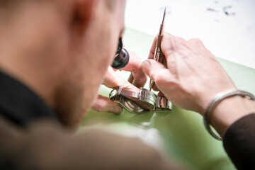 Watch maker repairing a classic watch, authentic work place. Using a monocle and small tiny tools for repairs