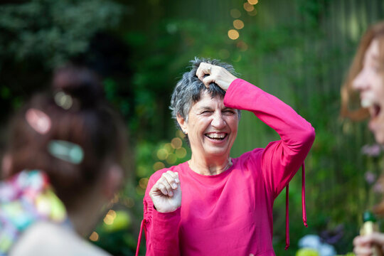 A mature woman laughing with friends and family at a summer garden party