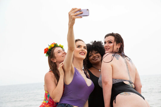 Mixed group of female friends having fun at the beach taking selfies.