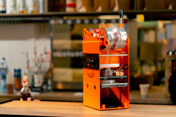 close-up of orange machine for packaging drinks with plastic on the bar counter