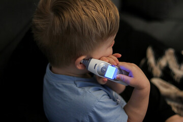 Close-up of toddler kid holding a digital thermometer and measuring his fever, blurry background