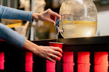 close-up of hands near the bar counter pouring lemonade into red paper glass