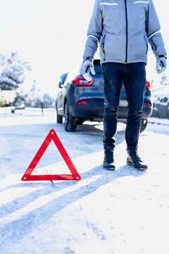 Broken car concept. Man with warning triangle on road covered with snow.