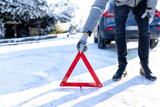 Broken car concept. Man placing warning triangle on road covered with snow.