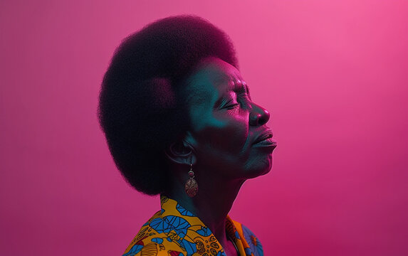 A multiracial woman with an afro hairstyle stands confidently against a vibrant pink backdrop.