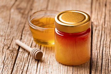 Honey in a jar and in a bowl, a wooden dipper on a wooden background, close-up.