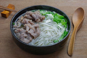 close up view of homemade style rice noodle with beef clear soup and vegetable in a ceramic bowl on wooden table. asian food menu.