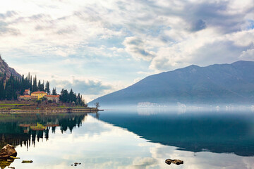 Bay of Kotor (Boka kotorska) on cloudy misty day. Calm water and sky reflected in water surface....