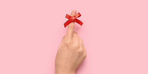 Female hand with red bow on index finger against pink background. Reminder concept