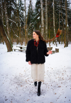 Beautiful extra long braided hair girl in Ukrainian traditional dress, black fur coat and red beads posing in winter forest . Portrait of young attractive stylish woman on winter background.

