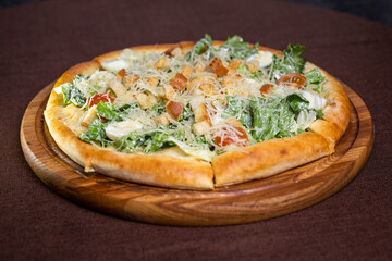 pizza with lettuce, tomatoes, cheese, croutons and egg on a wooden board. Brown background.