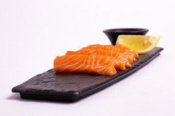 Salmon fillet with lemon and soy sauce on black stone plate, top view close-up.