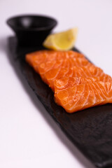 Salmon fillet with lemon and soy sauce on black stone plate, top view close-up.