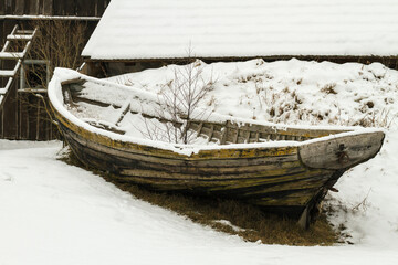 Abandoned boat by the barn in winter.