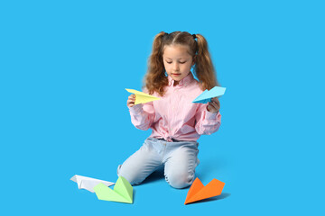 Cute little girl with paper planes on blue background