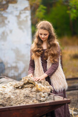 Portrait of beautiful blonde curl girl in medieval dress and fur vest on  nature. Young worker in...